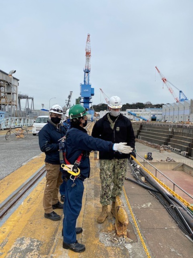 Yuuki Toya, center, Ship Repair Facility and Japan Regional Maintenance Center’s (SRF-JRMC) fall protection subject matter expert discusses the fall protection requirements and issues working at the dry dock’s edge with Capt. Neil Sexton, right, SRF-JRMC commanding officer.