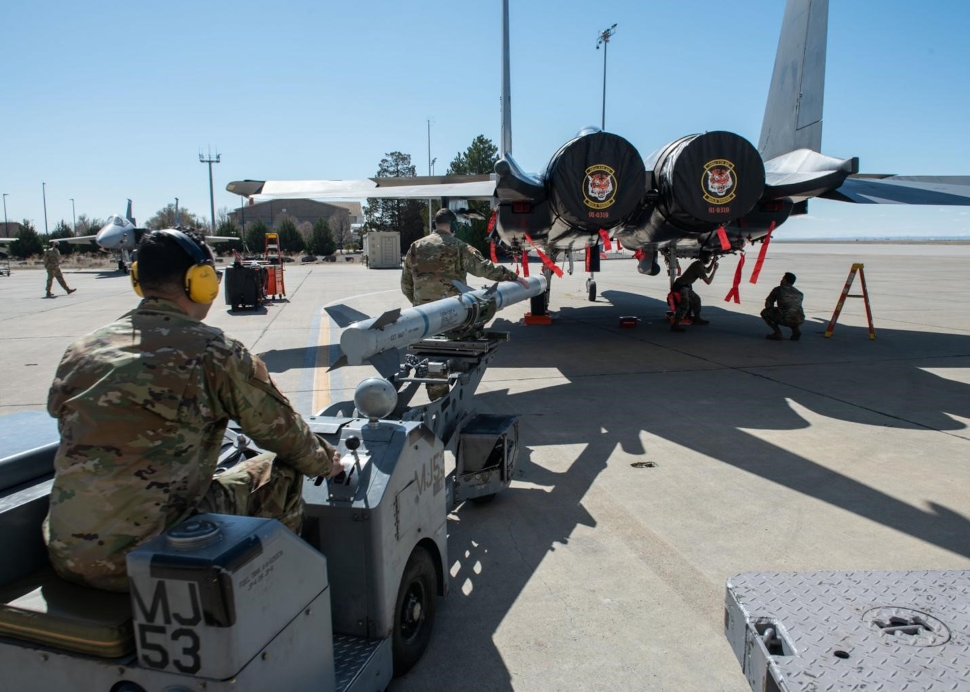A Airman drives a jammer vehicle that is holding a Air Intercept Missile to an F-15E Strike Eagle, with the assistance of his wingman.