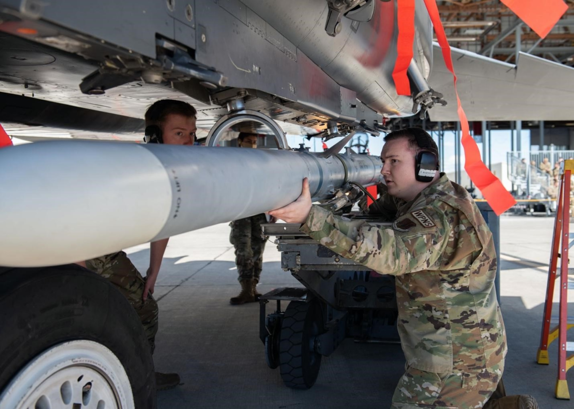 A Airman supports his three-man team in loading an Air Intercept Missile to an aircraft.