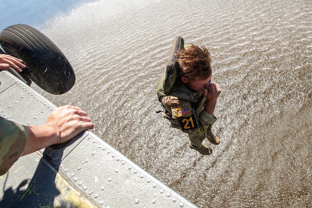 A solider jumps from a helicopter into a pond.