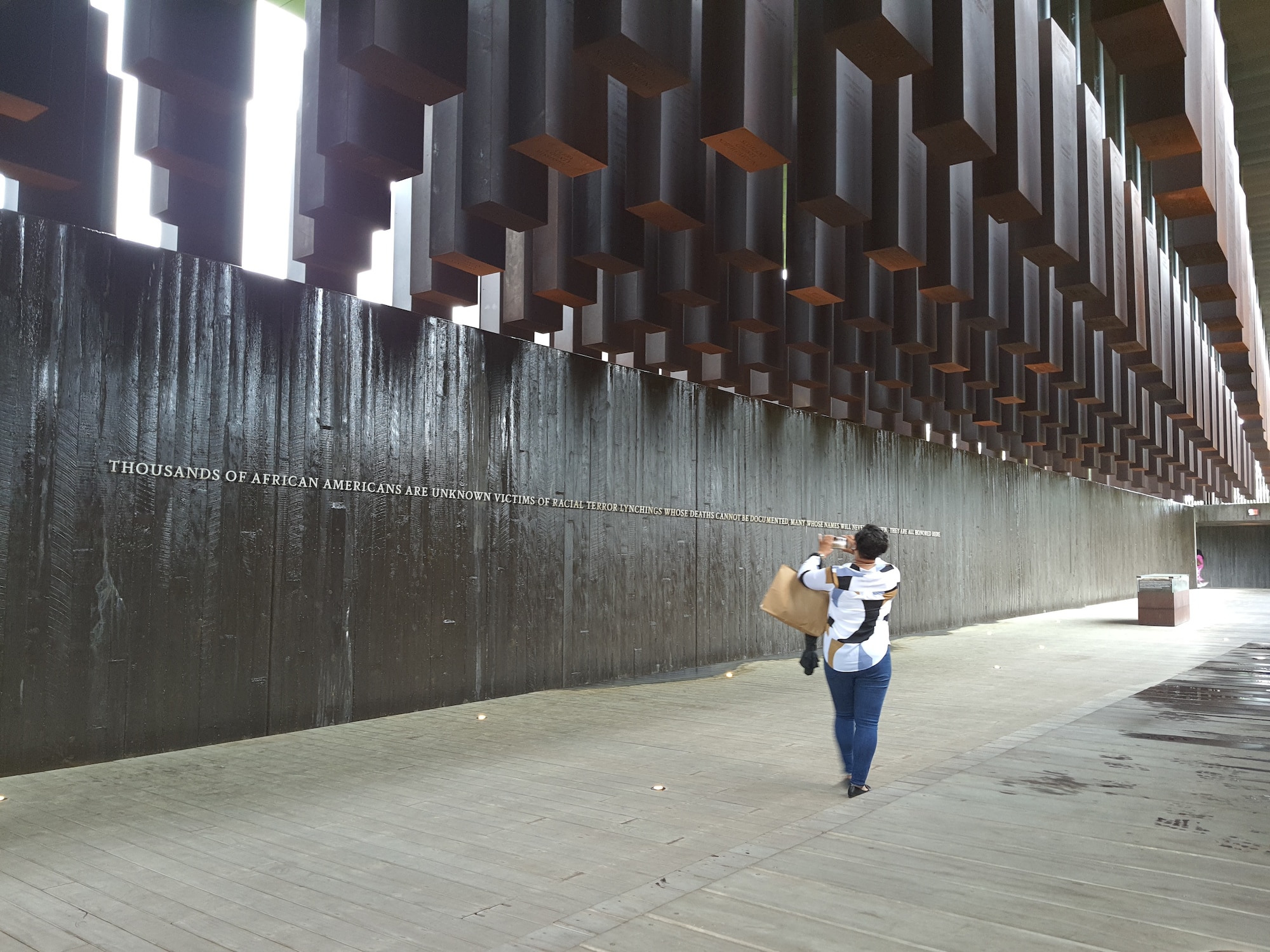 Senior Master Sgt. Tonya Taplin, 403rd Logistics Readiness Squadron plans superintendent, takes a photo of a quote on the wall of the National Memorial for Peace and Justice while walking below the six-foot tall steel columns which hung suspended overhead, each marked with a county, state, and the lynching victims' names, April 9, 2021 during the 403rd Mission Support Group leadership staff ride. Members of the 403rd MSG leadership participated in a non-traditional staff ride, which involves walking a battlefield, only in this case the battle that was fought was the Civil Rights Movement for African Americans in Montgomery, Alabama. The staff ride was intended to provide the leadership team with a better posture in order to have the tough conversations with their Airmen when it comes time to discuss diversity and inclusion and why it plays a vital role in combat readiness. (U.S. Air Force photo by Jessica L. Kendziorek)
