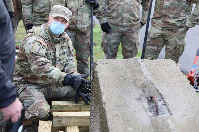 A soldier demonstrates lifting technique as older soldiers watch.