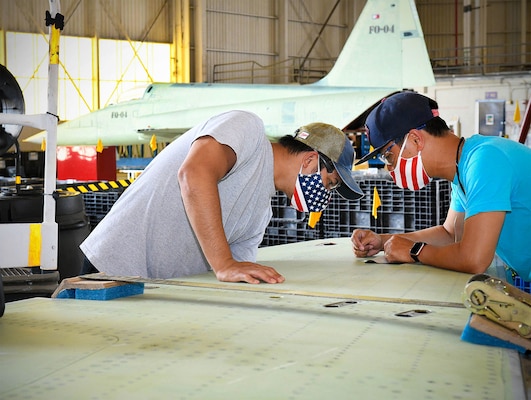 Fleet Readiness Center Southeast (FRCSE) F-5 production line aircraft mechanic, Mark Sta Maria, left, and work lead, Chanh Doan, check the wing pylon hole of an F-5N Tiger II fighter for corrosion.