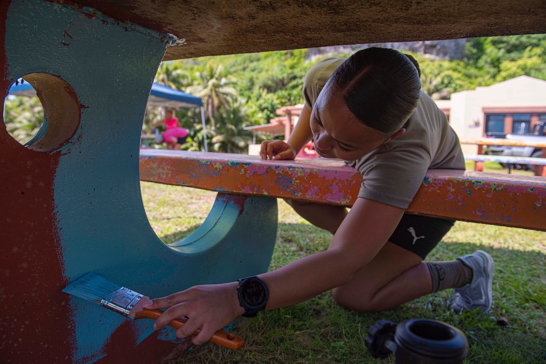 A military spouse paints a picnic table blue.