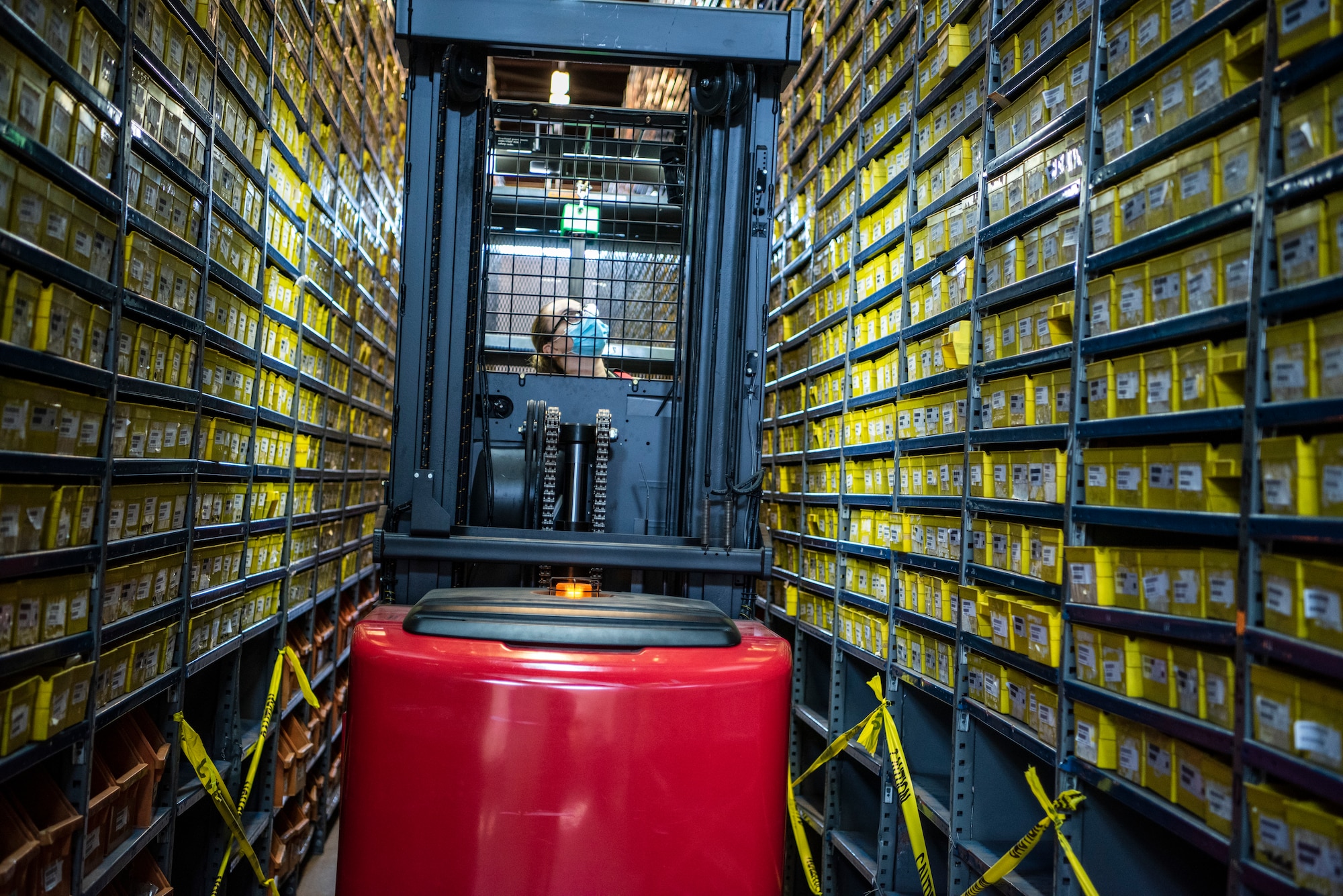 A female Airman drives a forklift through narrow shelves of small parts.