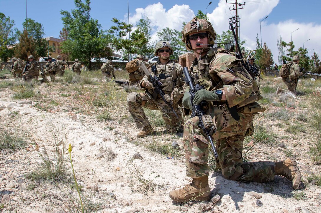 Soldiers with rifles kneel on the ground.