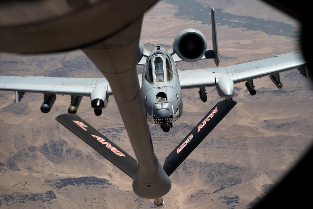 One aircraft approaches the refueling boom of another, high over desert terrain.