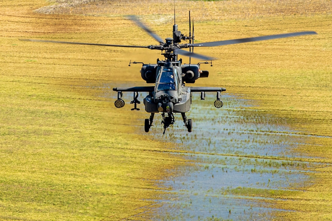 A helicopter flies over a swampy field.