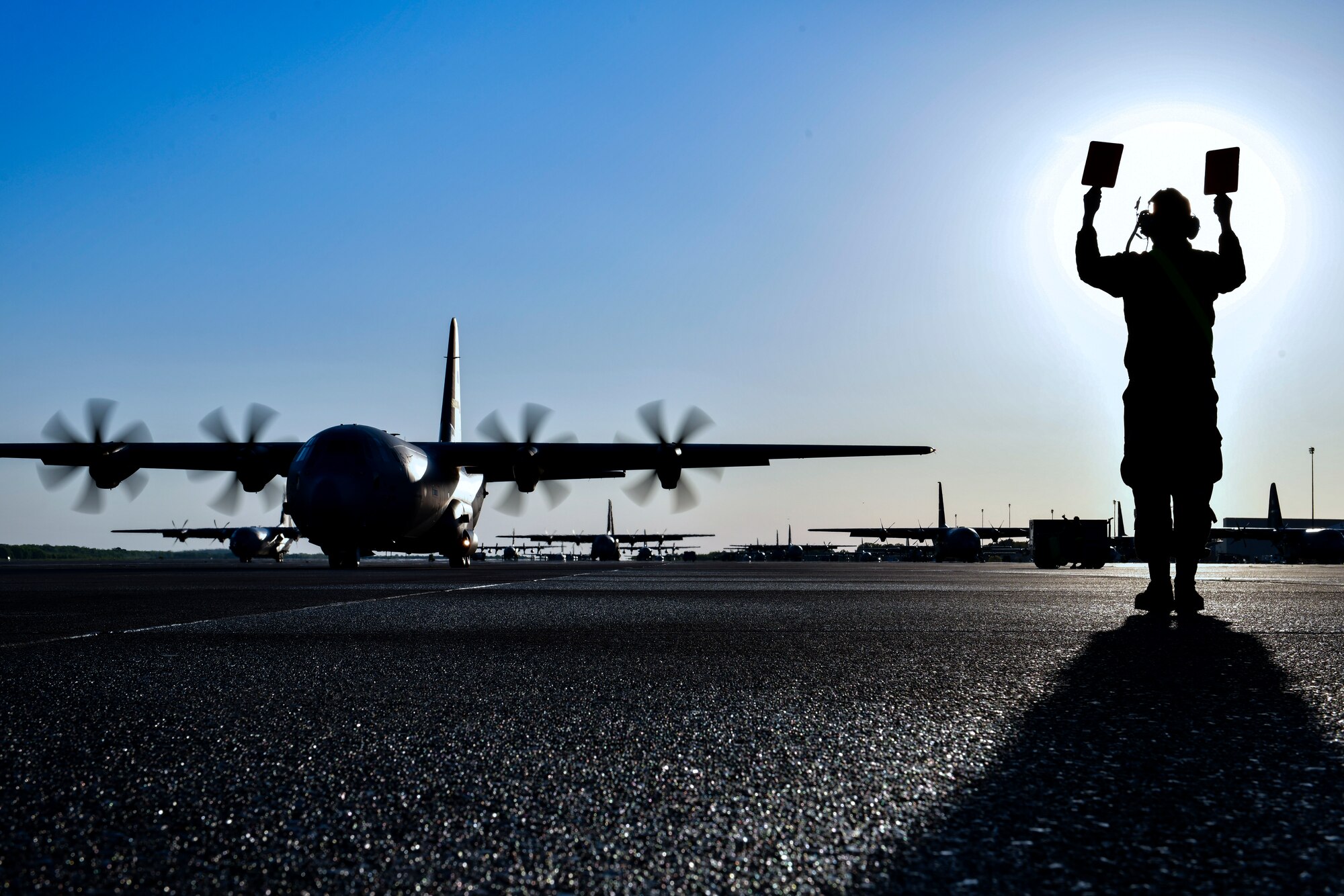 A crew chief marshals out a C-130J
