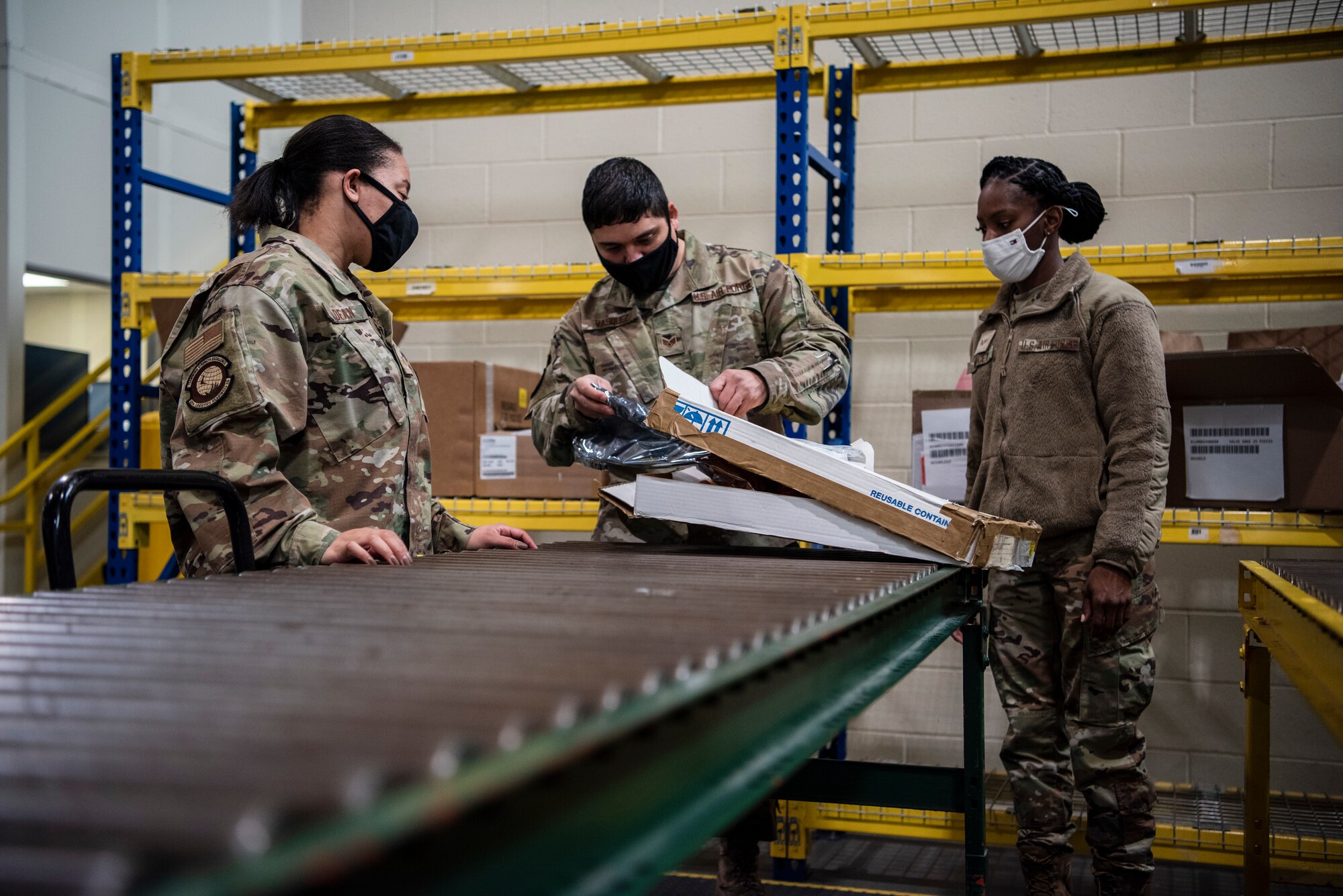 Three Airmen look at a box holding an aircraft part that needs to be repaired.