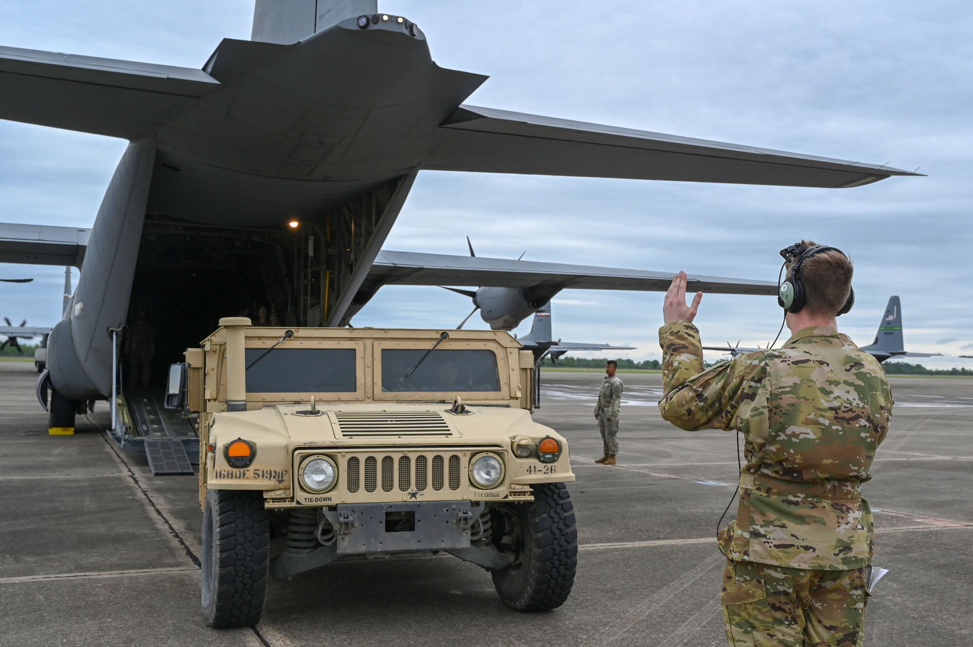 A loadmaster directs a humvee onto a C-130J