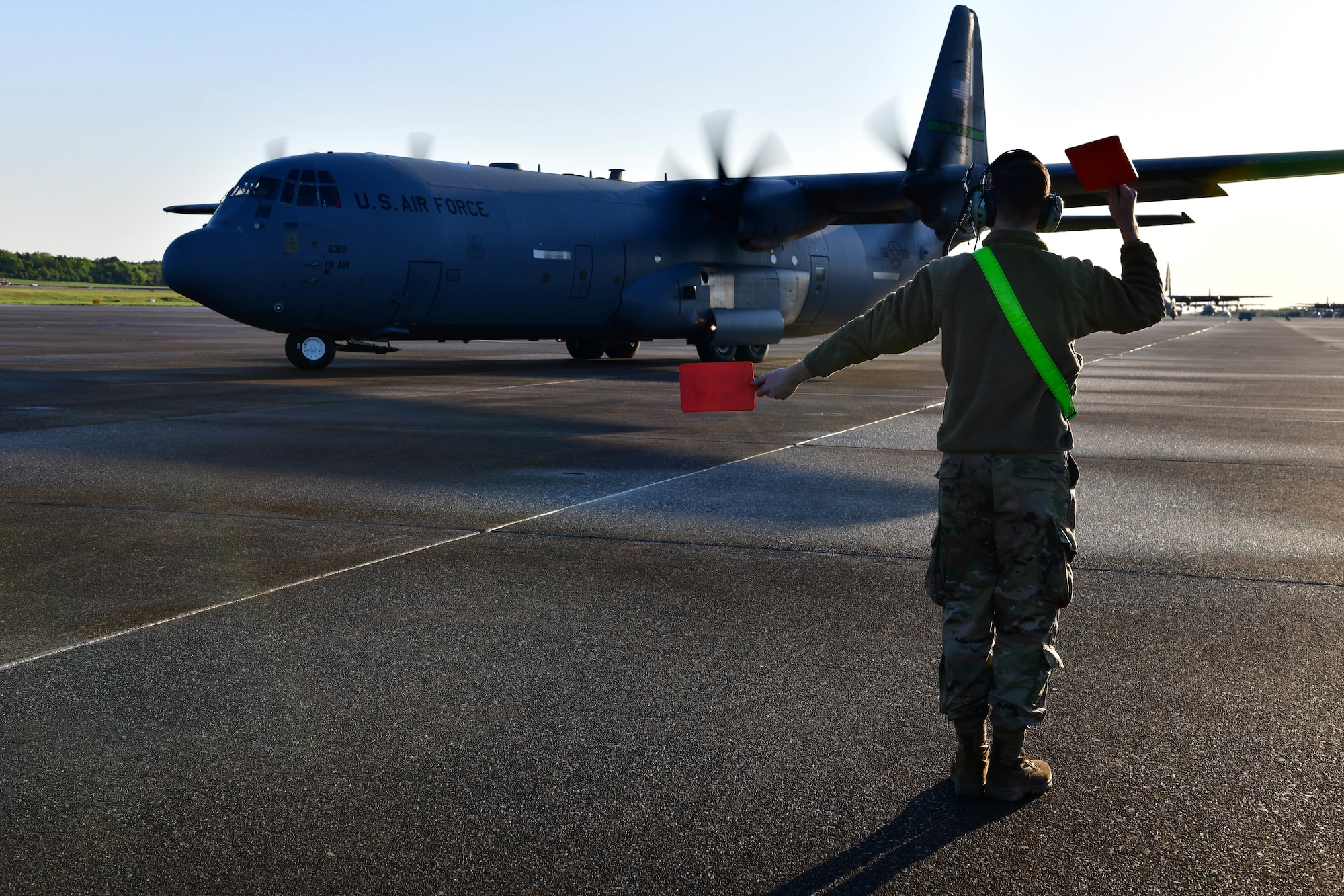 A crew chief marshals out a C-130J