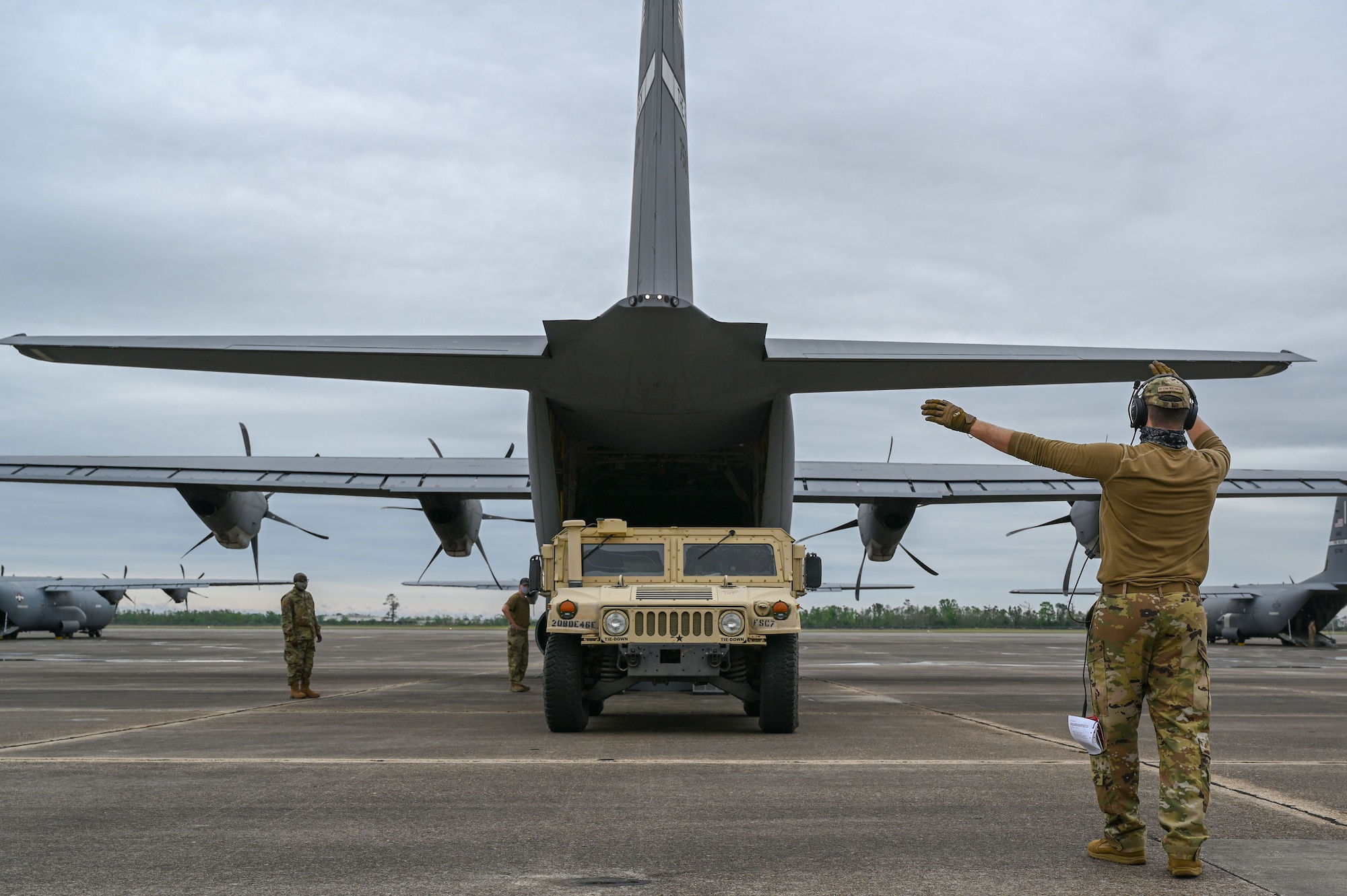 A loadmaster directs a humvee onto a C-130J