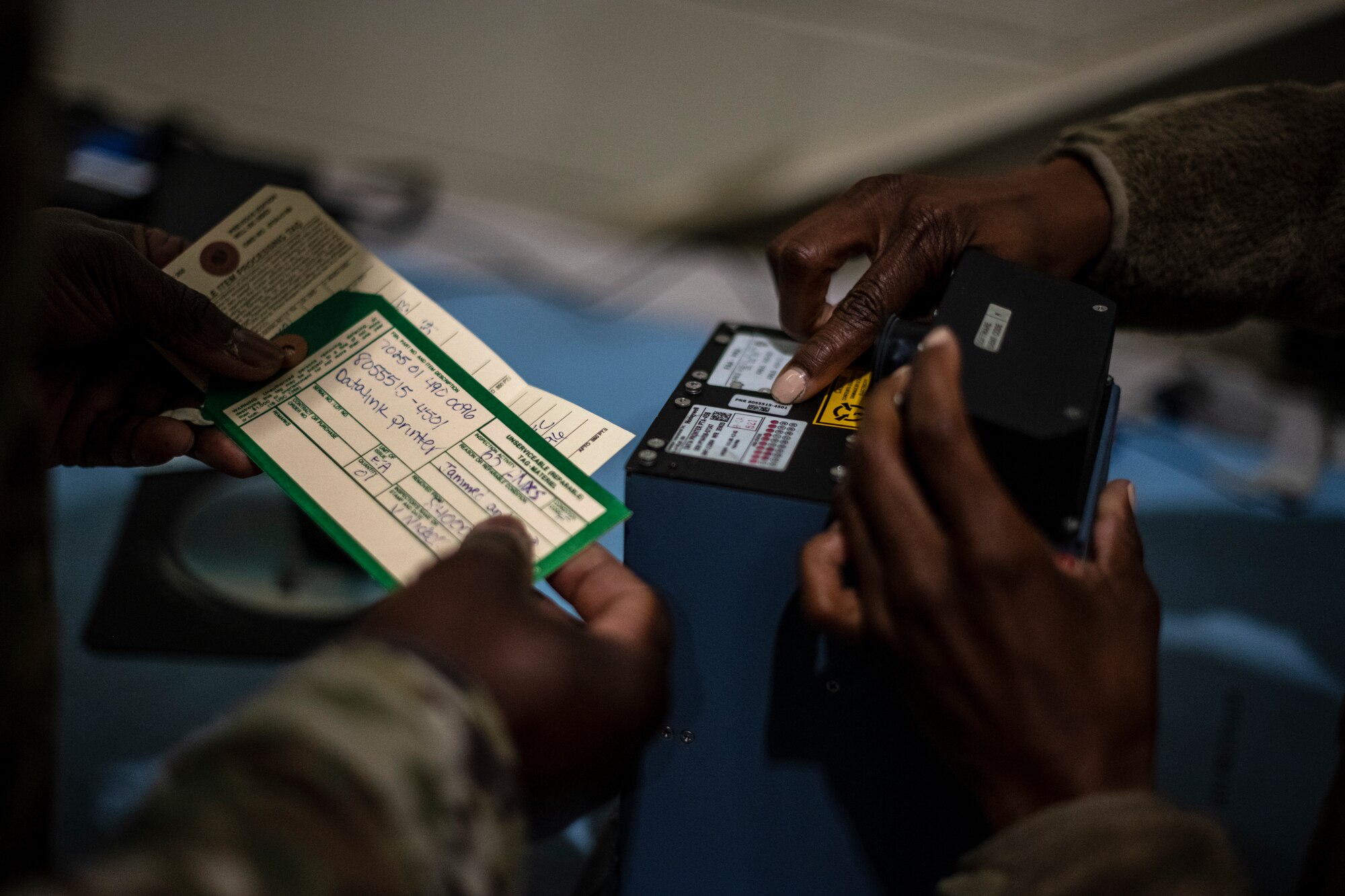 The hands of two Airmen are seen holding parts and inventory sheets.