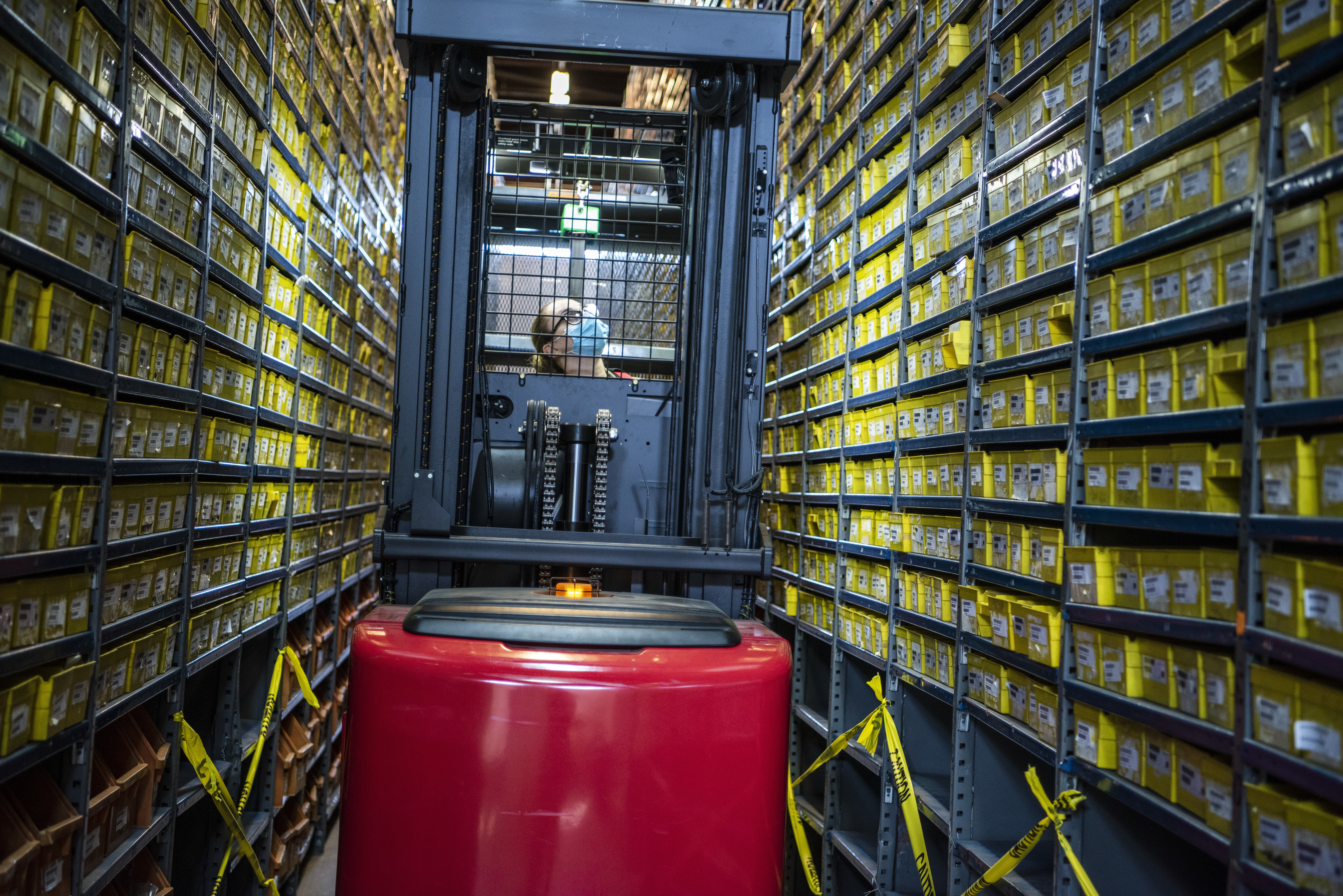 A female Airman drives a forklift through narrow shelves of small parts.