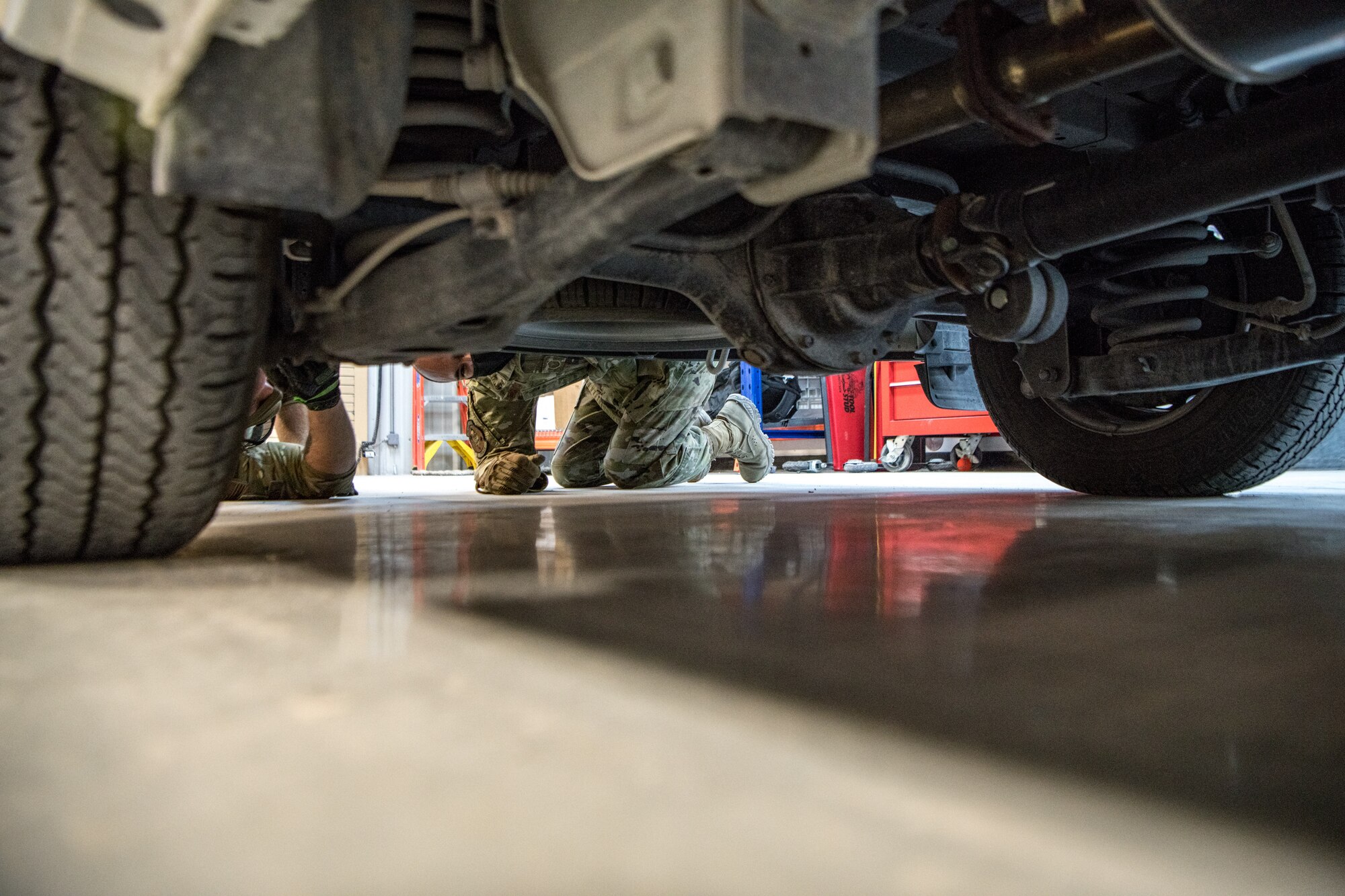 an airman inspects the undercarriage of a vehicle