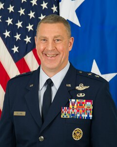 Maj. General Sullivan in uniform standing in front of the U.S flag and 2-star general flag.