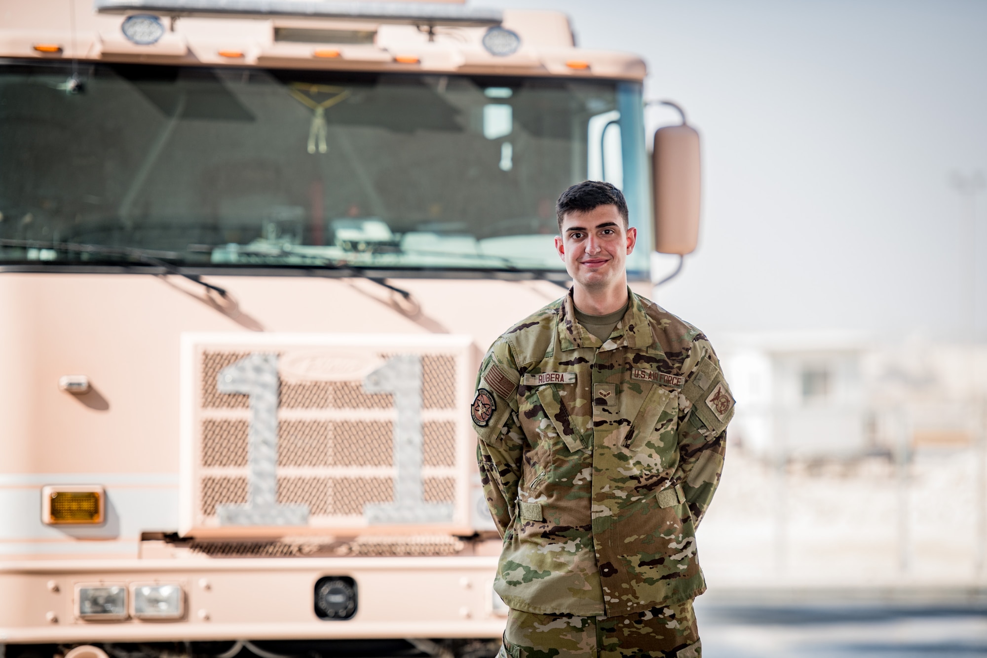 An airman poses for a photo in font of a firetruck
