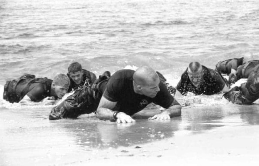 Marines crawl from the water onto a beach.