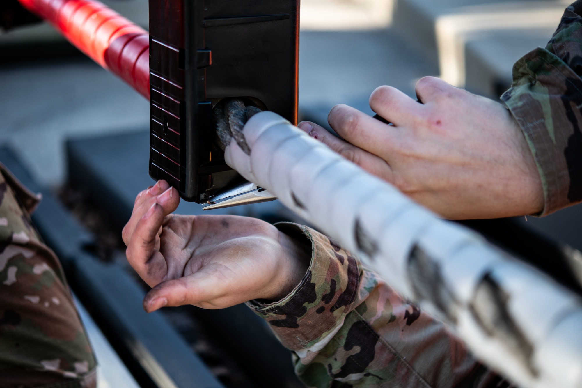 Senior Airman James Wolfley, 436th Civil Engineer Squadron electrical power production journeyman, inserts a metal wire into an encasing for a ground automobile retractable barrier (GRAB) net, at Dover Air Force Base, Delaware, April 3, 2021. The power production team conducts monthly maintenance on the GRAB net to ensure it functions properly in case of an emergency at the main gate. (U.S. Air Force photo by Senior Airman Marco A. Gomez)