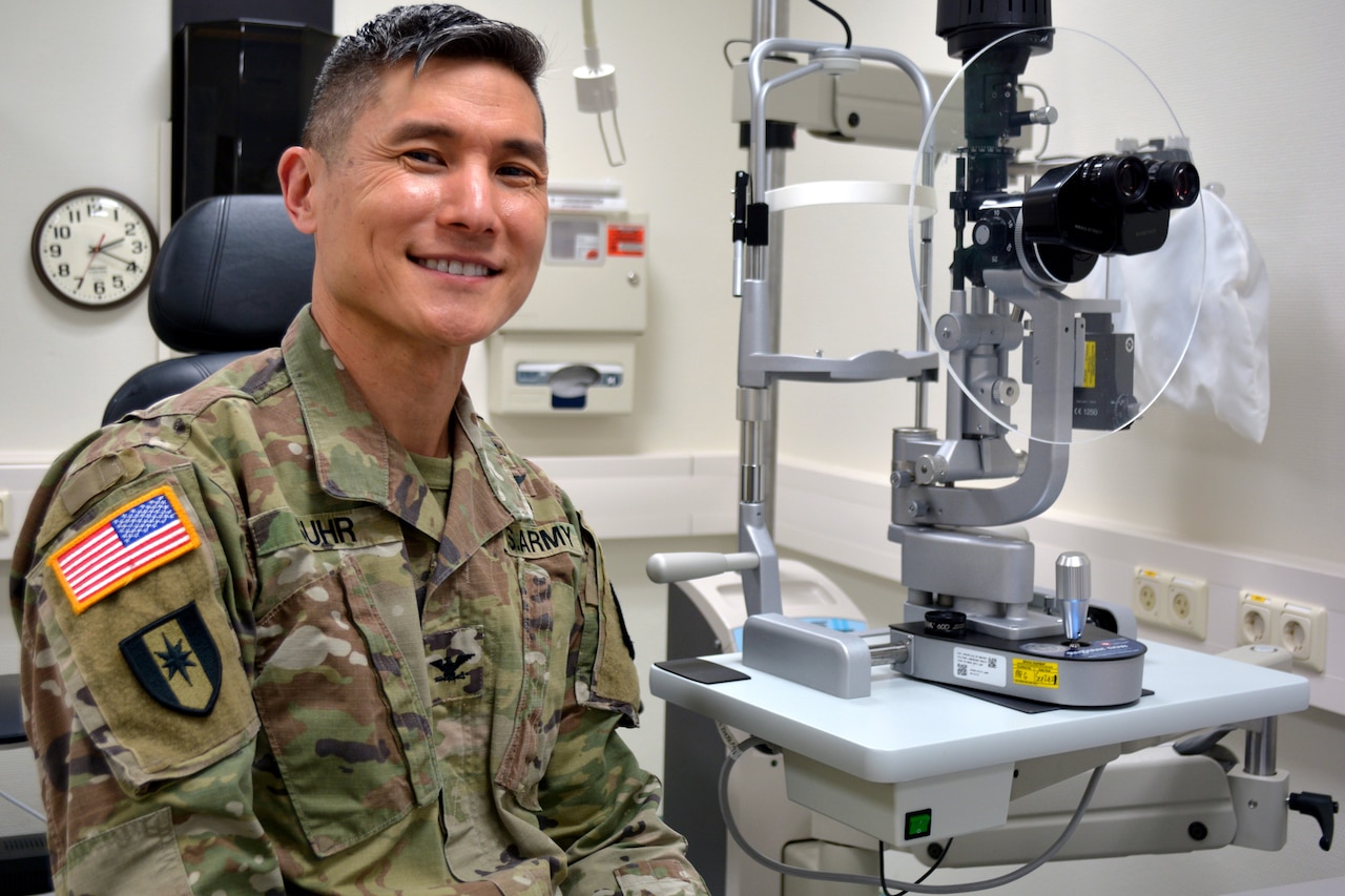 A soldier smiles for a photo while sitting by medical equipment in an office.