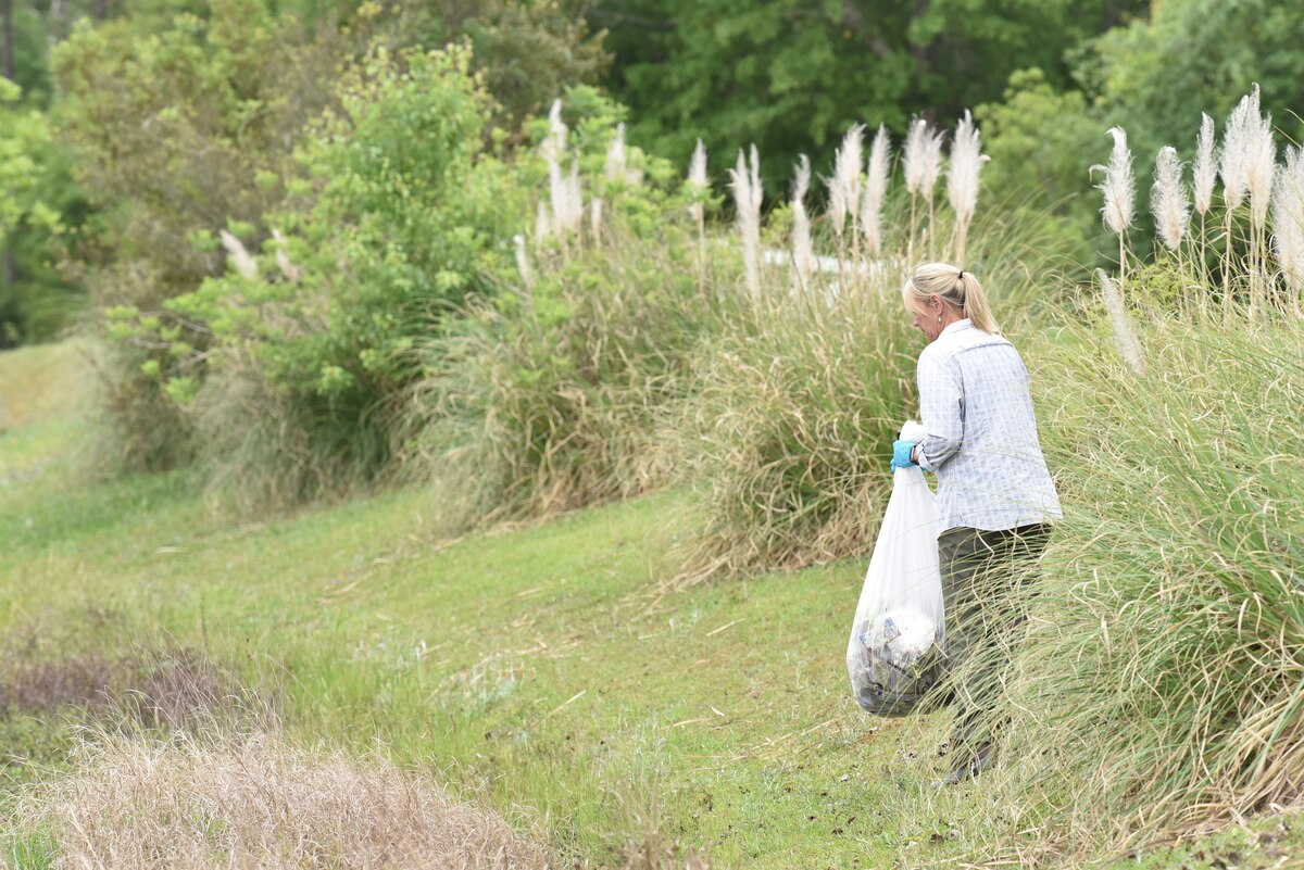 Photo shows woman picking up litter next to a lake.