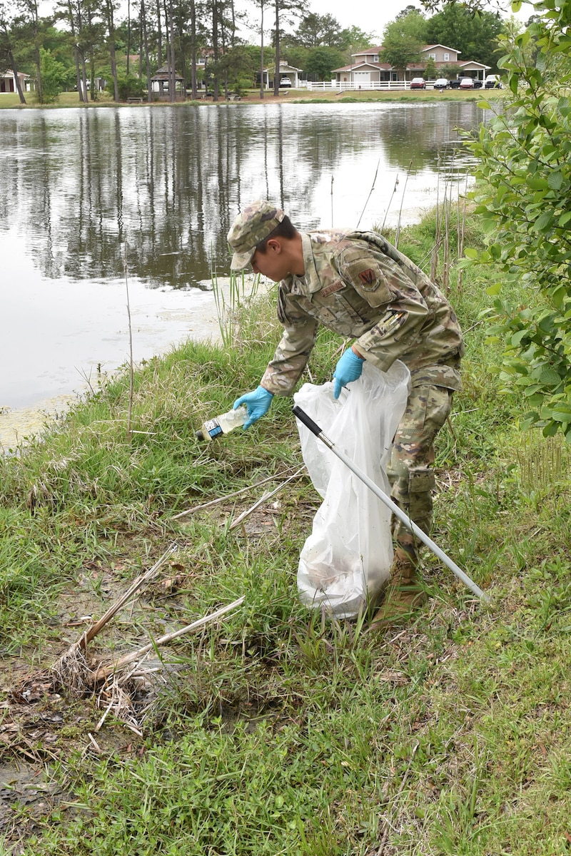 Photo shows Airman picking up litter next to lake.