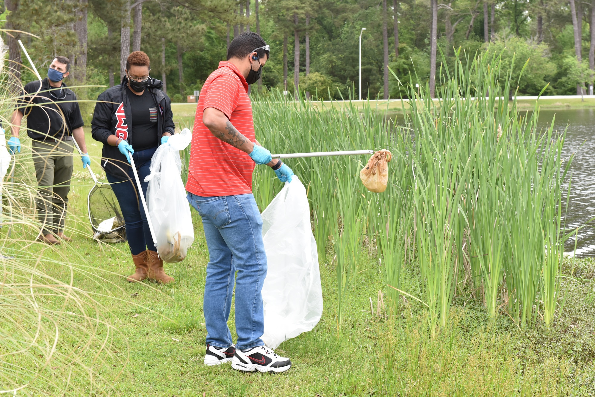 Photo shows three people pick up litter along the side of the lake.