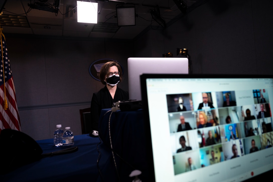 A woman sits at a desk and looks at a computer screen.