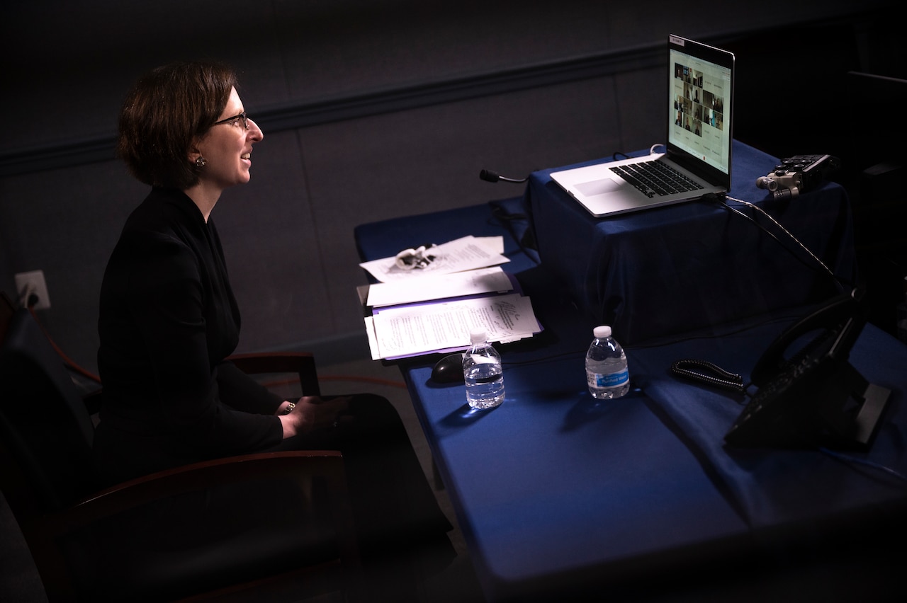 A woman sits at a desk and looks at a computer screen.