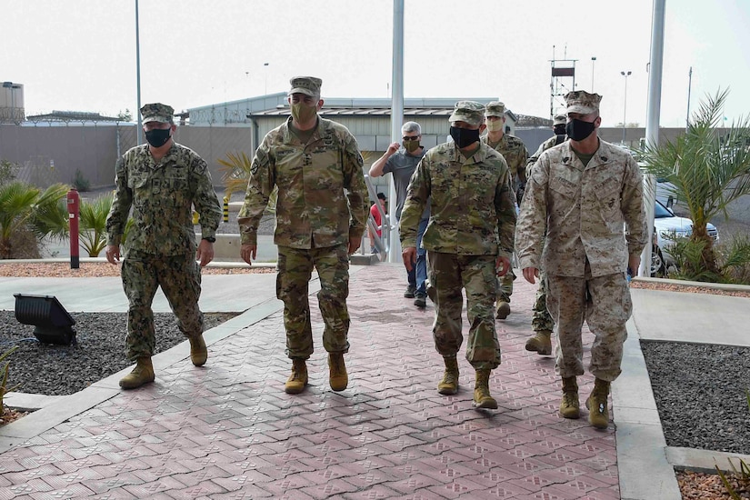 Four men in military uniforms walk into a building.