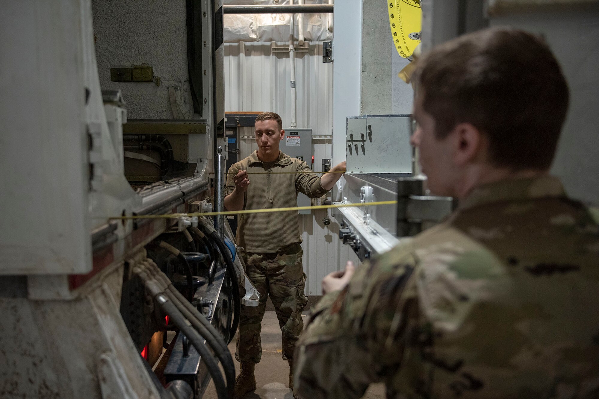 Two Airmen measure the distance with tape measures two transporter vehicles before the start of a missile roll transfer.
