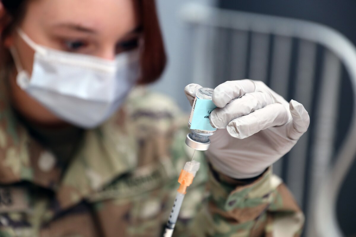 A medic draws a vaccine from vial with a syringe.