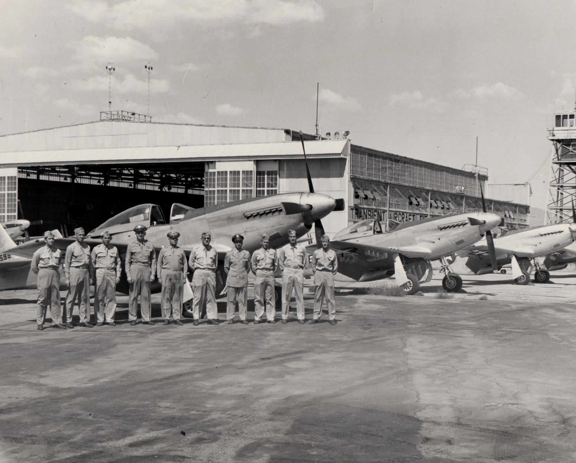 10 Airmen stand next to each other on a flight line in front of three planes and a hangar
