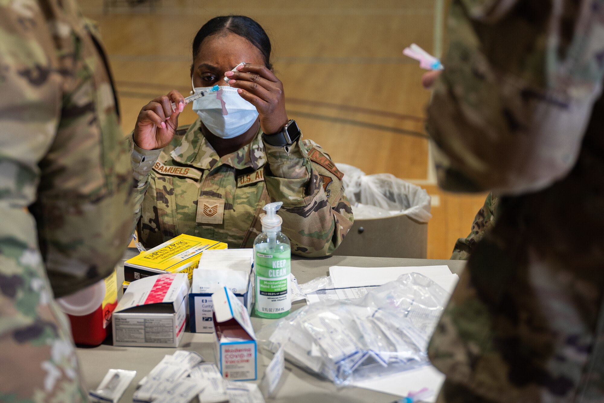 A woman in a military uniform carefully fills a medical syringe from a vial.
