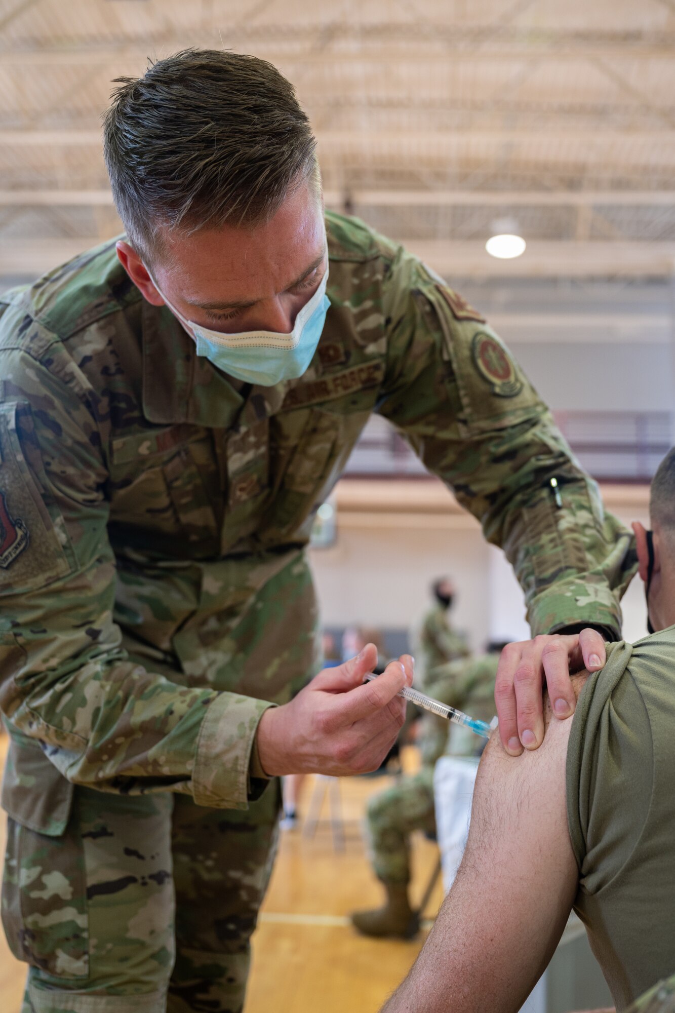 A man in a military uniform injects a syringe into the arm of a patient.