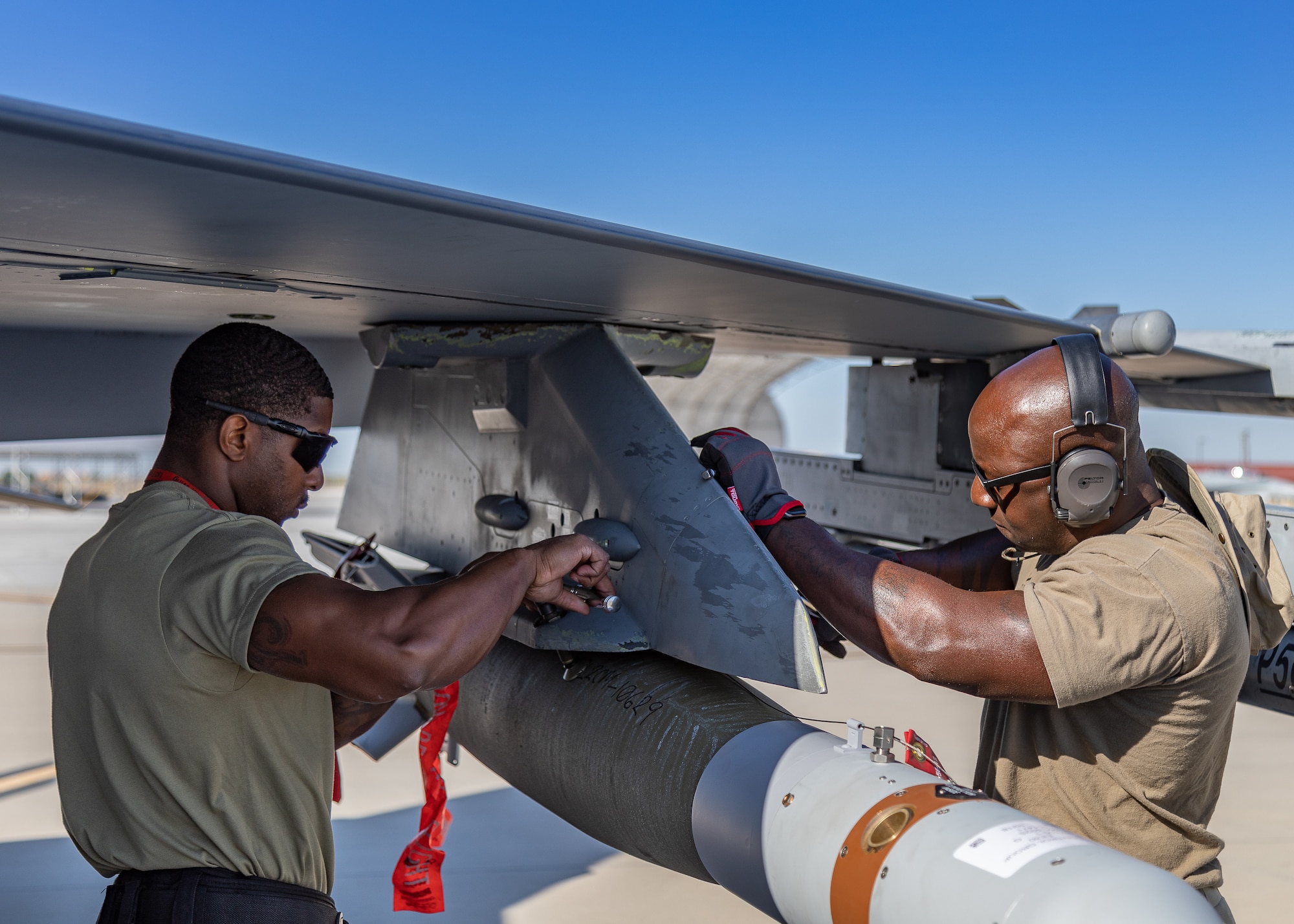 Two airmen attach a GBU-12 Paveway II bomb to the wing of an F-16 Fighting Falcon.