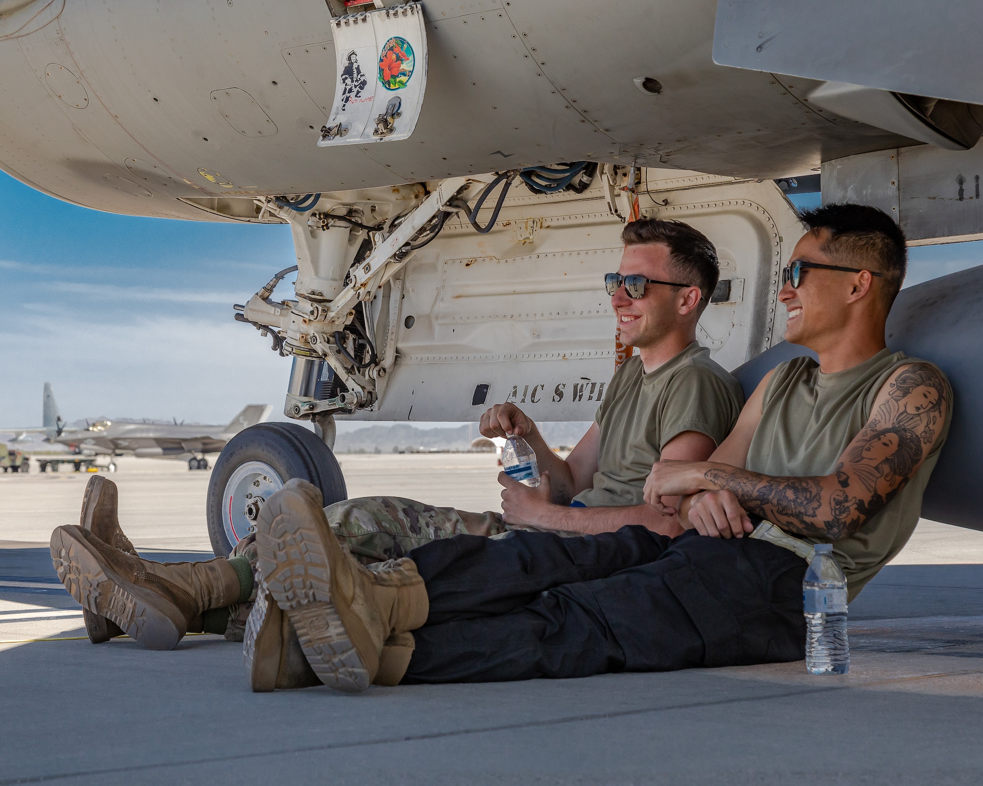 Two airmen sit and drink water underneath an F-16C+ Fighting Falcon.