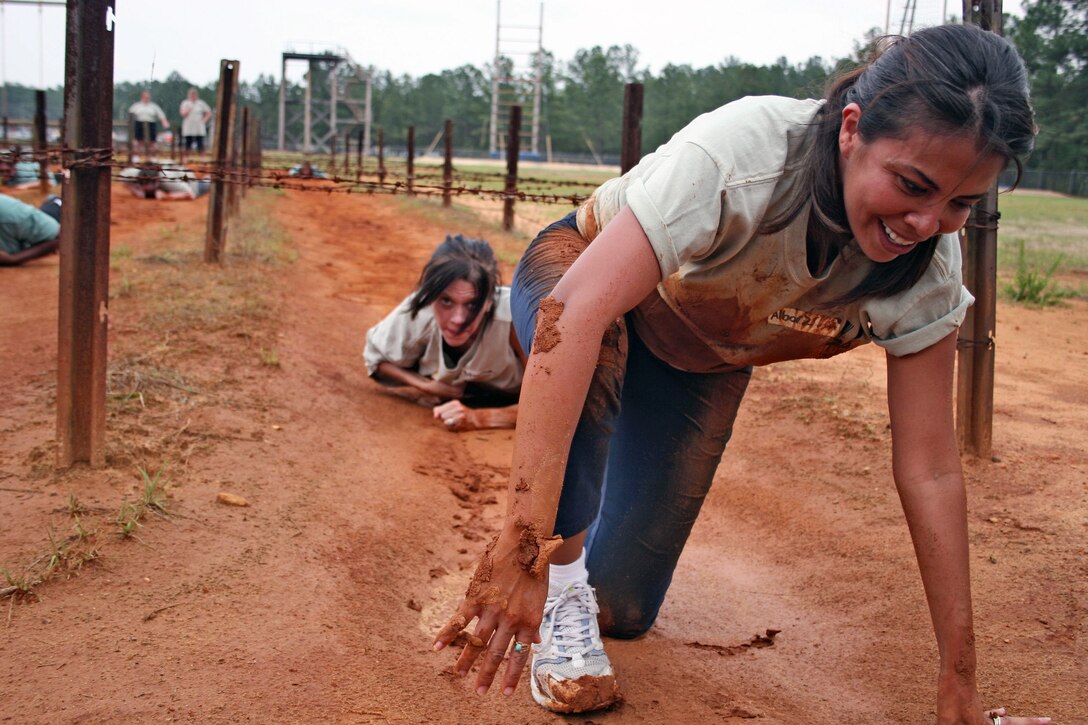 A smiling civilian begins to get up from a crawling position on a muddle obstacle course.