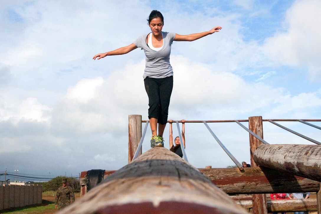 A person holds her arms out while walking on a raised horizontal log.