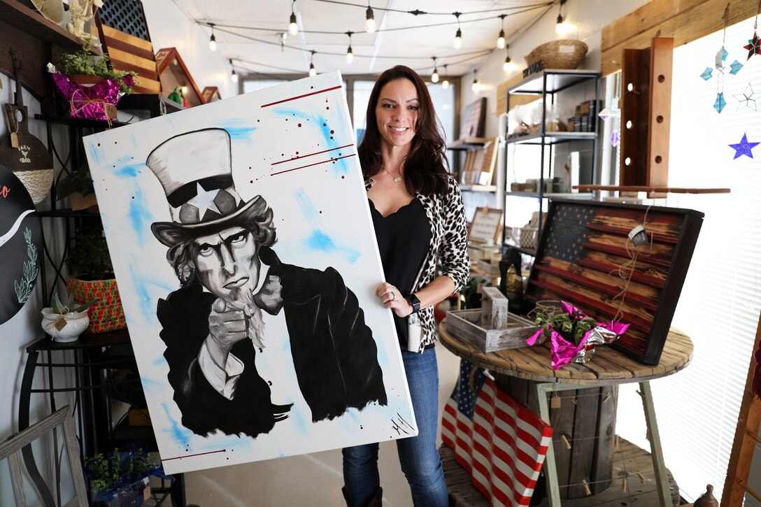 A civilian stands in a gift shop and holds up a drawing of Uncle Sam.
