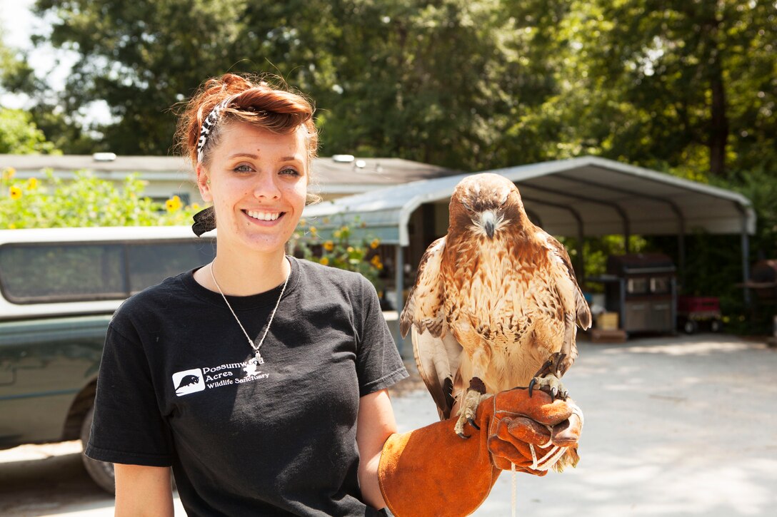 A Marine Corps military spouse smiles for a photo as she stands with a raptor perched on her gloved left arm.