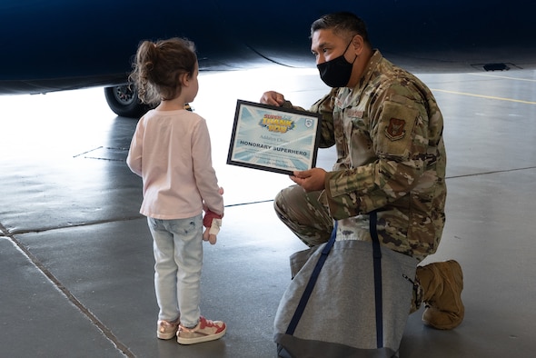 Kneeling Airman hands certificate to small child.