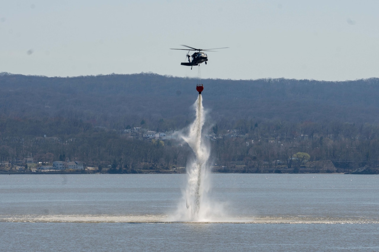 A helicopter dumps a bucket of water into a river.