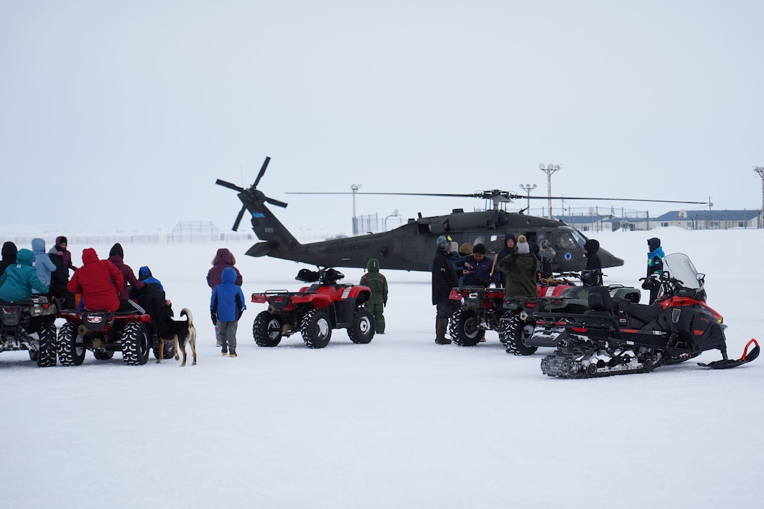 People mill about in the snow, There is a helicopter in the background.