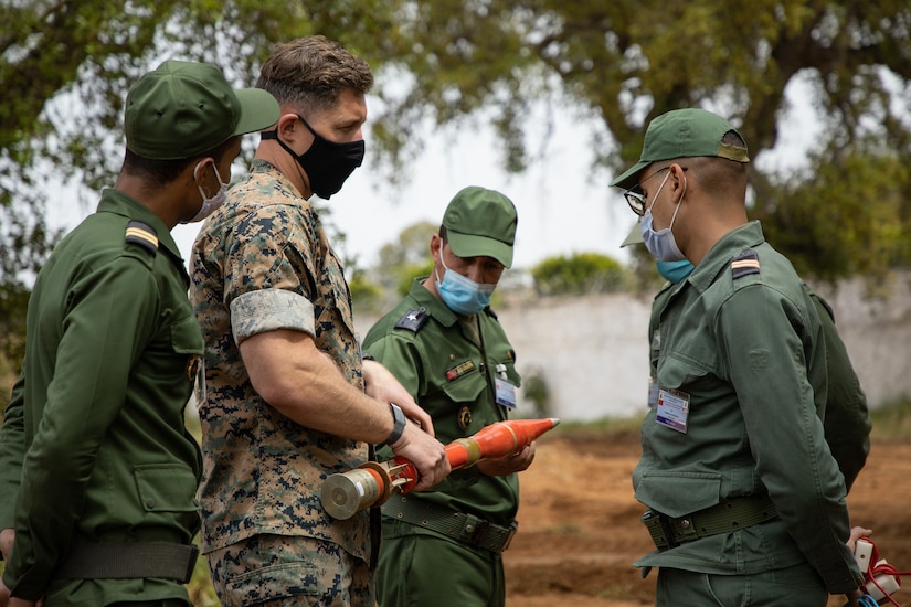 Soldiers in camouflage uniforms and face masks stand in a group during training.