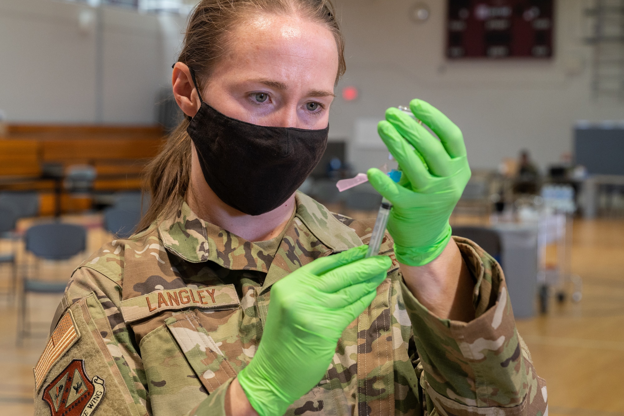 A woman in a military uniform carefully fill a medical syringe from a vial.