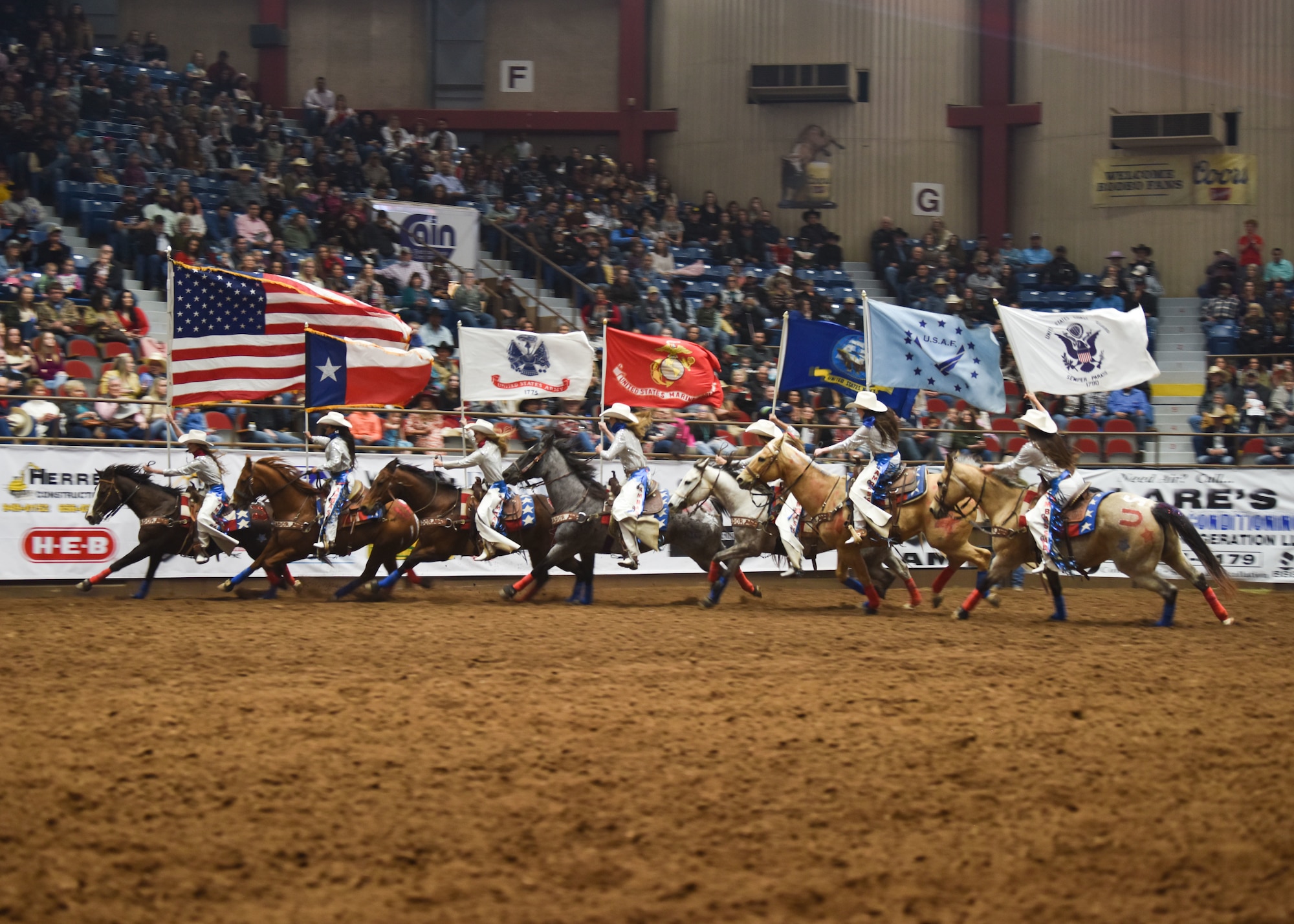 Rodeo participants ride around a rodeo ring holding U.S. service flags during Military Appreciation Night at the Foster Communications Coliseum, in San Angelo, Texas, April 21, 2021. The action was part of a long-standing tradition tied to this annual event. (U.S. Air Force photo by Staff Sgt. Seraiah Wolf)