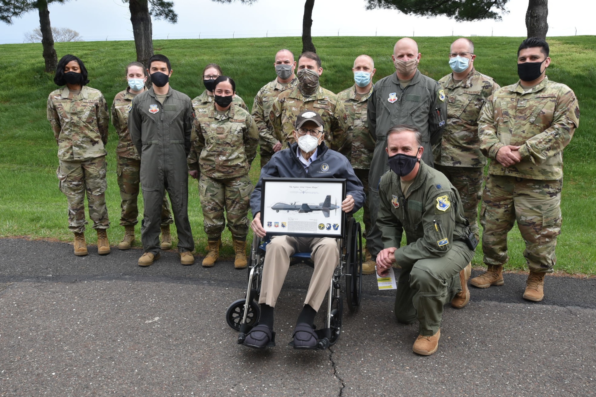 Air Force members pose for a photo with a World War II veteran sitting in a wheel chair holding a picture frame.