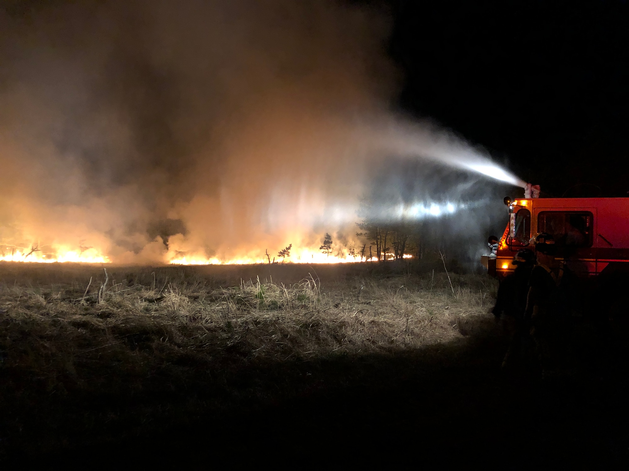A fire truck sprays water to douse a fire in a field.